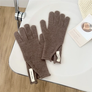 Detail of dark brown knitted five-finger gloves featuring a sewn-on white branded wool tag