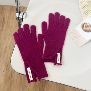 Close-up of magenta pink wool knitted gloves with stylish brand label on white table