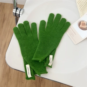 Macro shot of green knitted wool glove with white logo tag on a textured surface