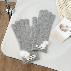 Detail of light gray knitted gloves with soft white pom poms and a letter tag on wrist