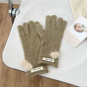 Detail of olive green knit gloves featuring beige pom-poms and brand labels for winter