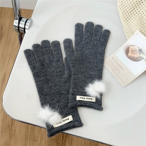 Close-up of dark grey knitted gloves featuring soft white pom-poms and brand label detail
