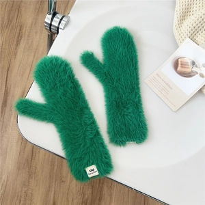 Detail of bright green faux fur mittens featuring a white brand woven label and plush texture