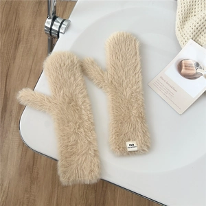 Close-up of beige plush mittens with fluffy texture and brand tag on a warm background