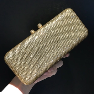 Detail of hand holding a luxury gold rhinestone clutch with elegant metal clasp