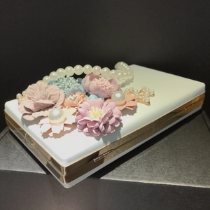 Detail of white evening clutch with 3D floral decorations and pearl handle chain
