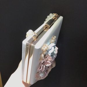 Detailed view of the white satin clutch featuring 3D floral accents and a pearl handle