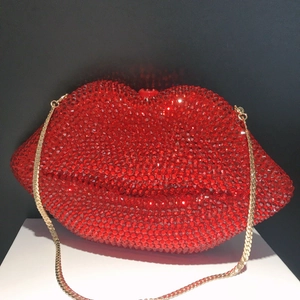 Sparkling red lip-shaped clutch bag with rhinestones and gold chain on white pedestal