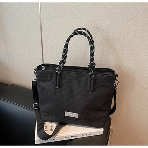 Détail du cabas en toile noire avec poignées en corde rayées et bandoulière amovible