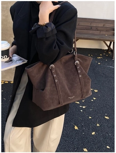 Détail d'un sac cabas en daim marron foncé avec sangles décoratives et boucles métalliques