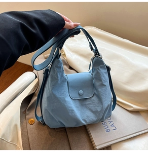 Nahaufnahme der blauen Nylon-Hobotasche mit feiner Textur und Druckknopf in der Hand