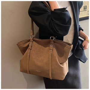 Brown leather tote bag side view with silver buckles on a model in gray blazer