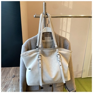 Detail of white grainy PU leather tote bag with silver eyelets hanging on a metal rack
