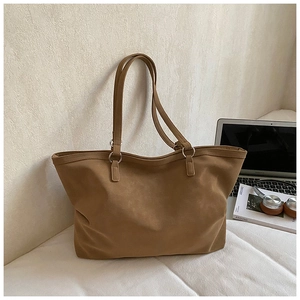 Detail of large brown tote bag with silver hardware on desk with laptop and gear