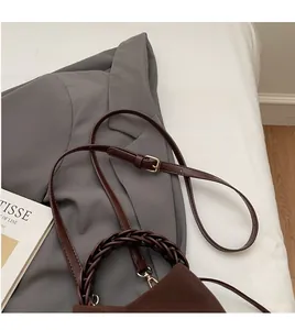 Detail of smooth leather bucket bag featuring a dark brown woven handle and adjustable strap
