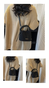 Detail of black leather bucket bag with braided handle and gold logo on front