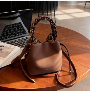 Detail of a brown leather bucket bag with a hand-woven handle and drawstring closure