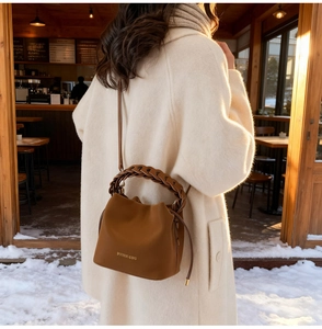 Detail of a brown PU leather bucket bag featuring a unique woven handle and gold branding