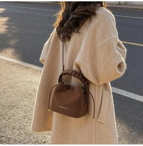 Detail of a brown leather bucket bag featuring a woven handle and gold brand lettering