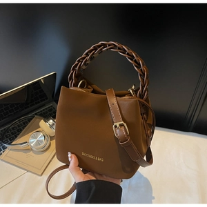 Detail of dark brown bucket bag featuring woven handle and gold brand lettering