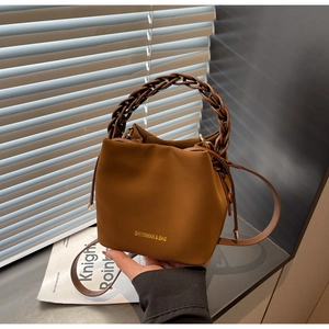 Detail of caramel brown PU leather bucket bag with a chunky woven handle and drawstring