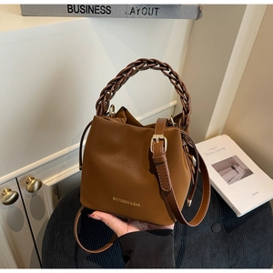 Detail view of brown PU leather bucket bag with wide woven handle and adjustable strap