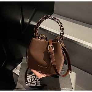 Close-up of matte brown PU leather bucket bag with woven chain handle and thin strap