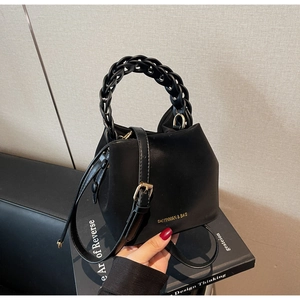 Close-up of black PU leather bucket bag featuring a woven chain handle and gold hardware