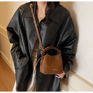 Detail of a brown PU leather bucket bag featuring a unique braided handle and gold logo
