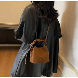 Brown PU leather bucket bag detail with woven handle and logo on black leather coat