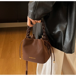 Detail of brown PU leather bucket bag featuring a woven handle and gold Shiyinman logo