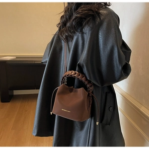 Detail view of dark brown pebbled leather bucket bag with braided handle and gold logo