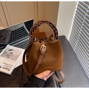 Detail of caramel brown PU leather bucket bag featuring a thick woven handle and metal buckle