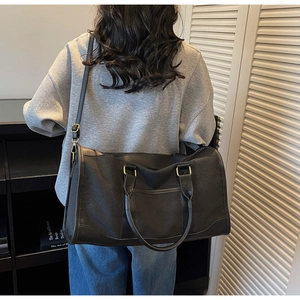Detail of a large black canvas tote bag with brown trim and adjustable shoulder strap