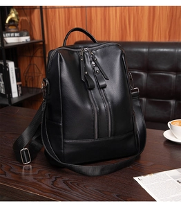 Close-up of black faux leather backpack with metallic zippers on a dark wood surface