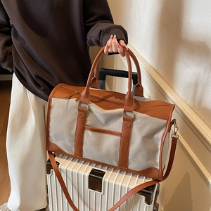 Large gray canvas tote bag with brown leather handles placed on a white suitcase