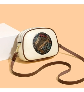 Close-up of beige embossed shoulder bag with dual gold zippers and brown leather straps
