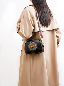 Detail of vintage black leather bag with colorful elephant relief worn with khaki trench coat