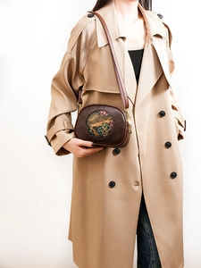 Close-up of brown leather bag with colorful elephant art pattern worn on khaki trench coat