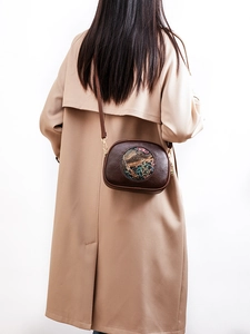 Brown leather crossbody bag with ethnic embossed elephant and floral patterns on a model