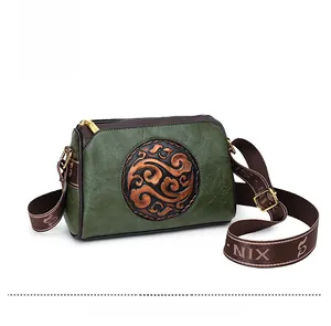 Detail of vintage embossed texture on olive green leather crossbody bag with brown trim