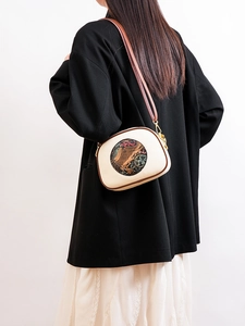 Detailed back view of a beige crossbody bag with ethnic elephant motif on a model