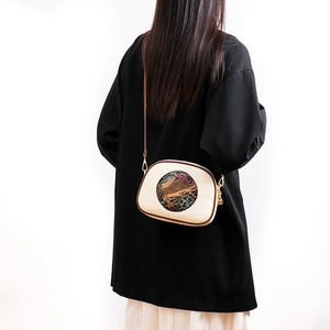 Detailed view of cream crossbody bag with vintage elephant pattern on model in black coat