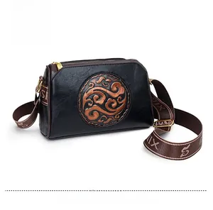Detail view of black faux leather crossbody bag featuring vintage embossed pattern and strap