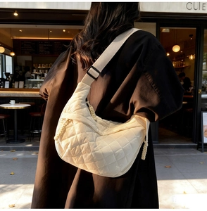 Close-up of beige quilted hobo bag with wide shoulder strap and woven zipper detail