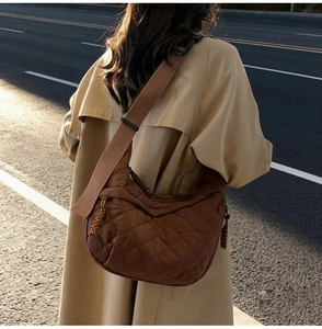 Outdoor street view of a brown quilted half-moon crossbody bag with adjustable strap