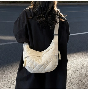 Close-up of white quilted half-moon crossbody bag with adjustable wide fabric strap