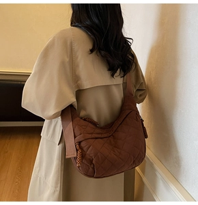 Detailed view of dark brown quilted crescent bag with diamond pattern on trench coat