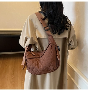 Detail of brown quilted half-moon crossbody bag featuring wide shoulder strap and brand label