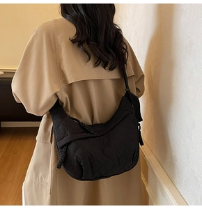 Detail of a black quilted crescent bag with diamond stitching worn on a beige coat
